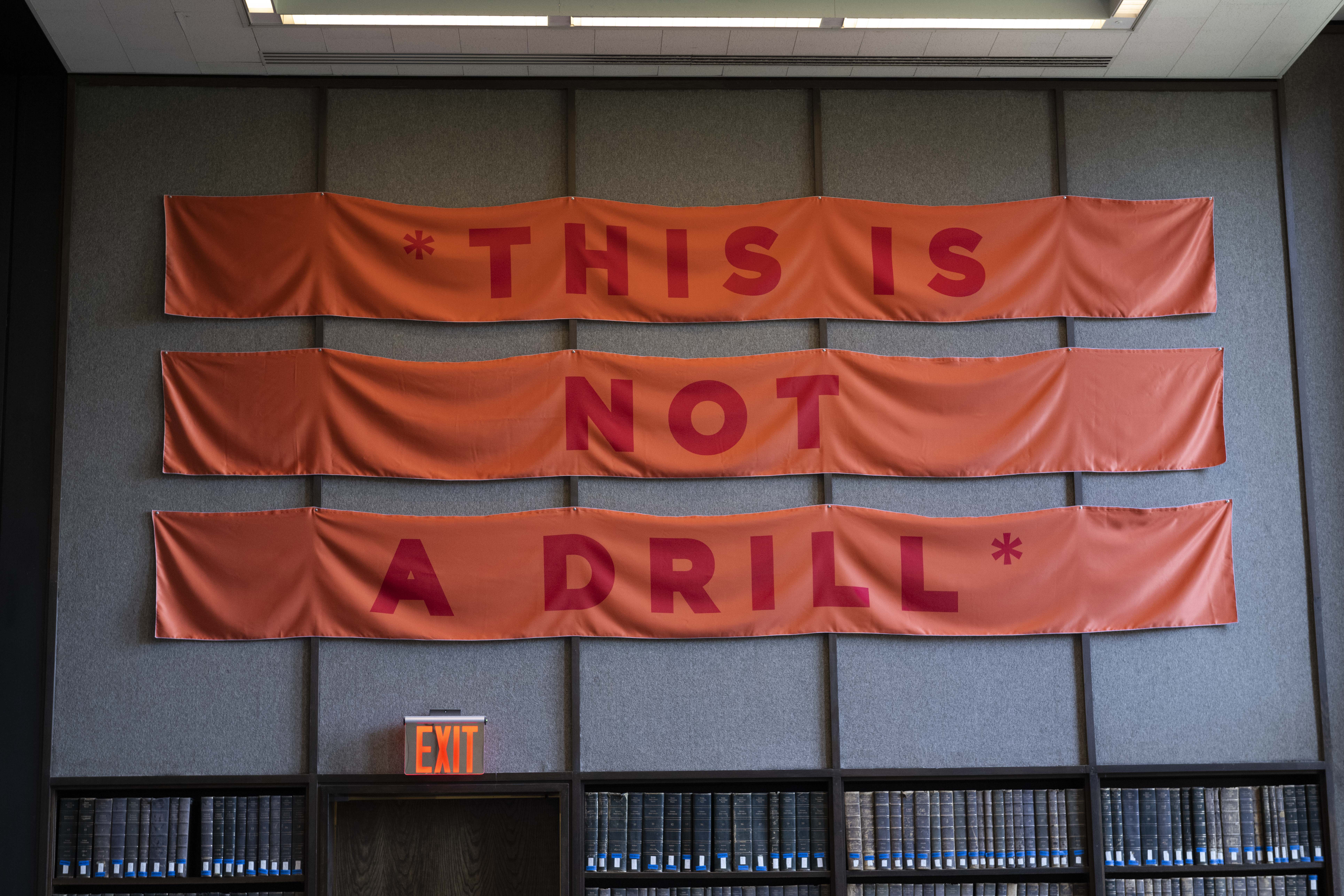 Photograph of orange banner with words *THIS IS NOT A DRILL* and bookshelves below