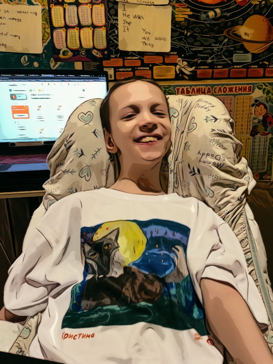 Ivan, a boy with open, smiling, and playful face is looking at the camera; he is sitting in a chair dressed in a white t-shirt with what seems like a naïve picture of wolf and full moon. Behind him, there is a on open laptop gleaming with light and rows of school-related rules and a poster of Solar system hanging on the wall.