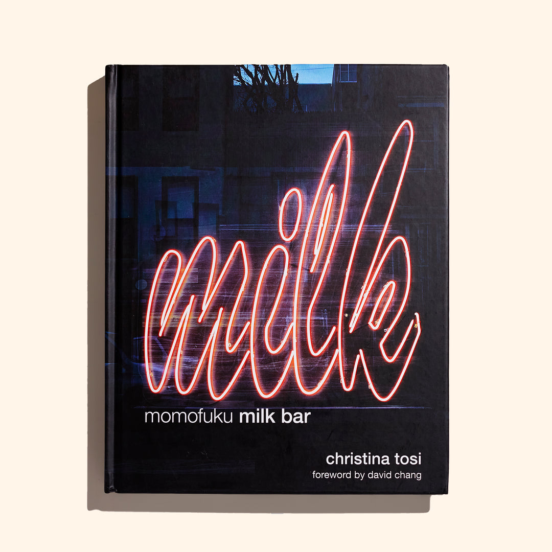 The cover is dominated by a pink, neon sign-like text that reads "Milk". Underneath and left-justified is the title in white lettering. The author's name appears to the bottom right. This is all against a background photo of what looks to be a city building at dawn or dusk.