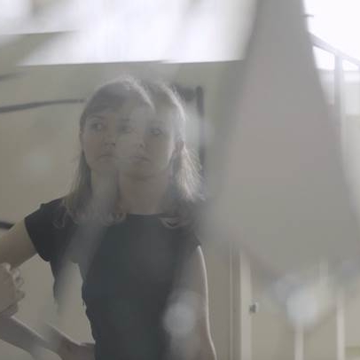 Desaturated, double exposure photograph of person with bangs and shoulder length hair, light-colored skin, wearing a dark t-shirt