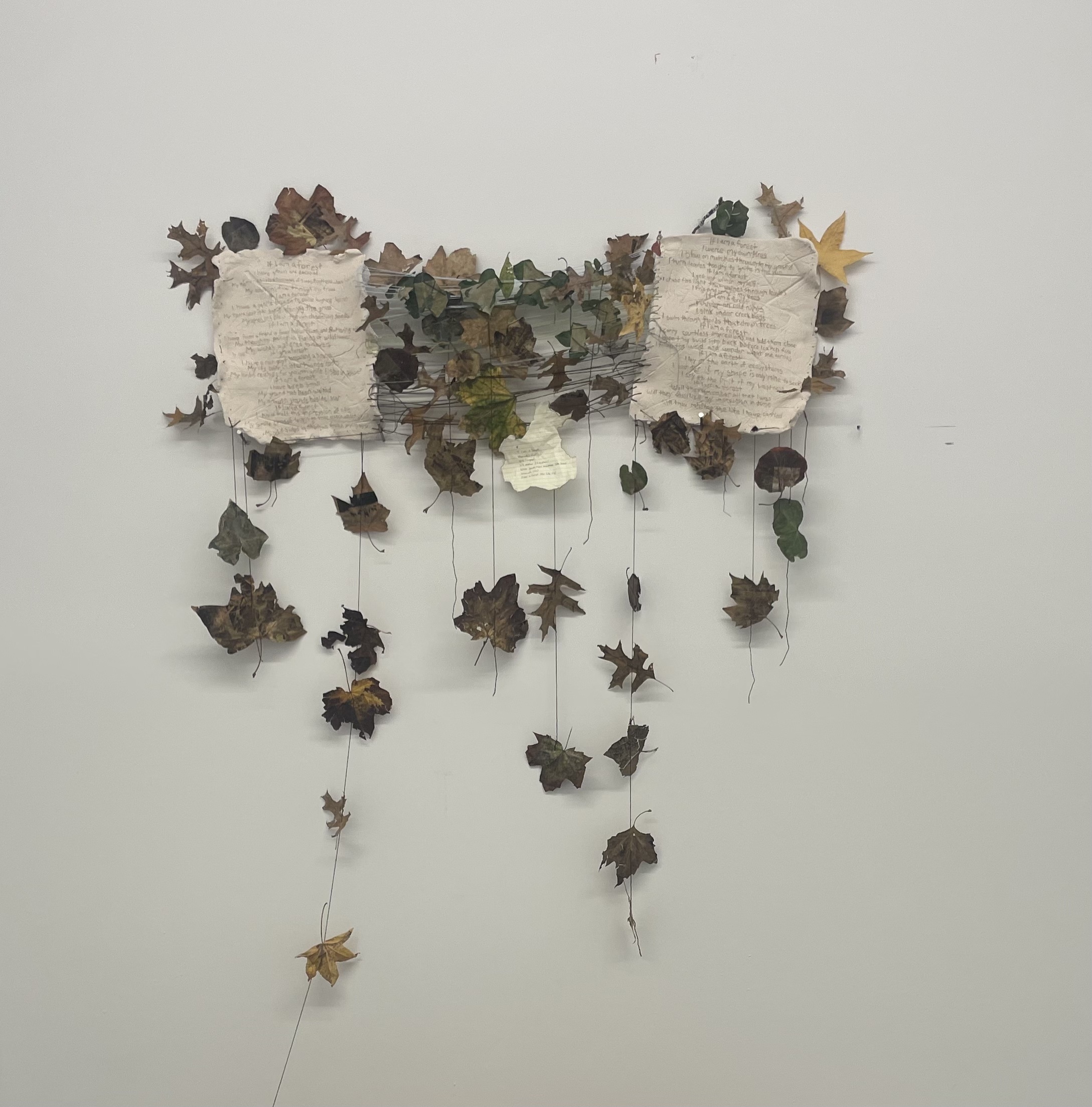 Image of hanging sculpture containing etched beige ceramic, brown leaves, and dark gray wire