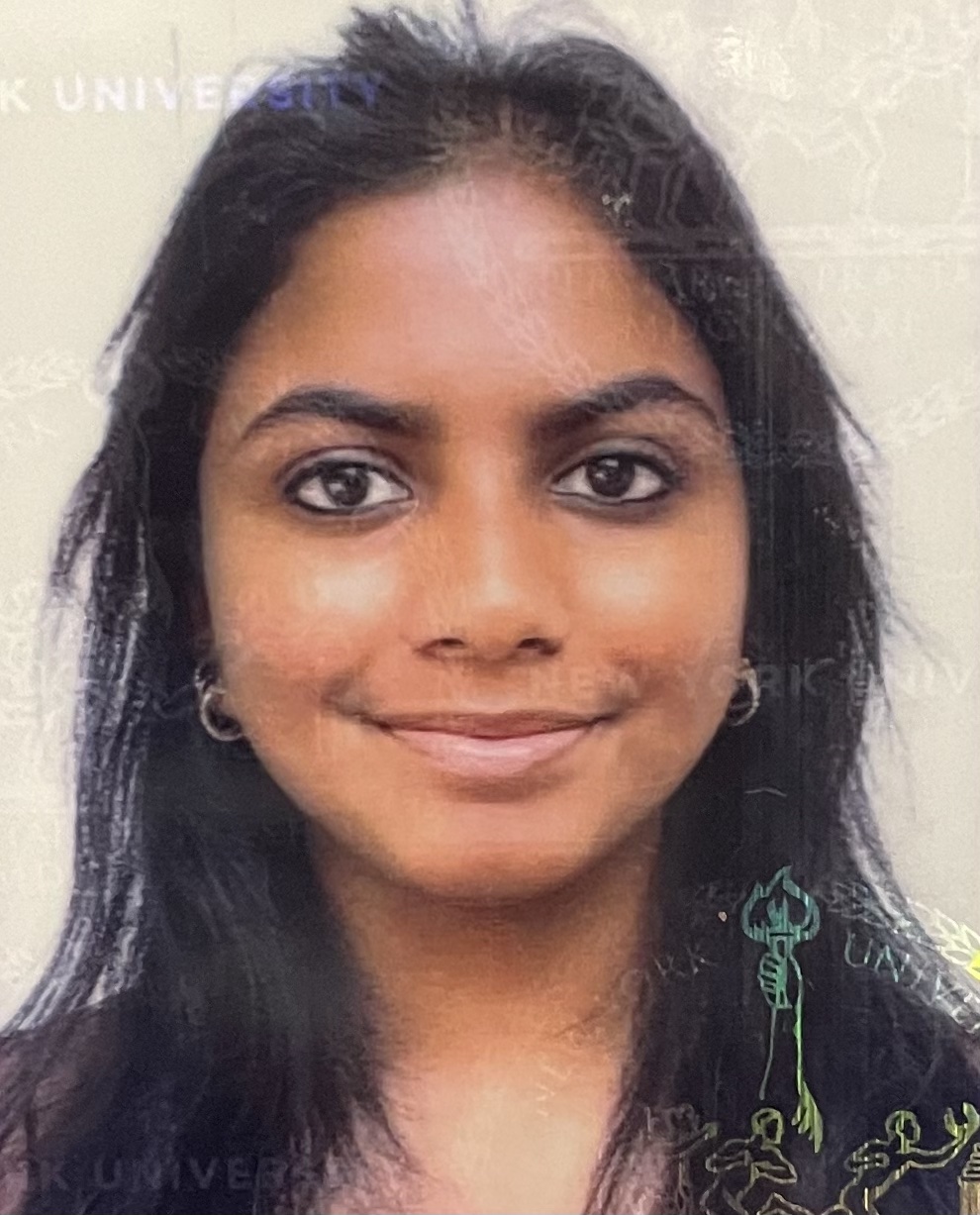 Photograph of a person with medium-colored skin and black hair, wearing silver hoop earrings against an off-white background