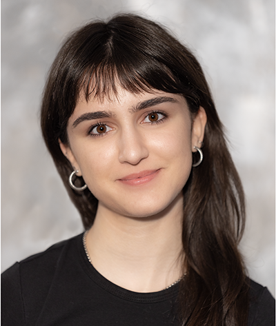 Photograph of person with long dark brown hair, light brown skin, wearing silver earrings and a black shirt