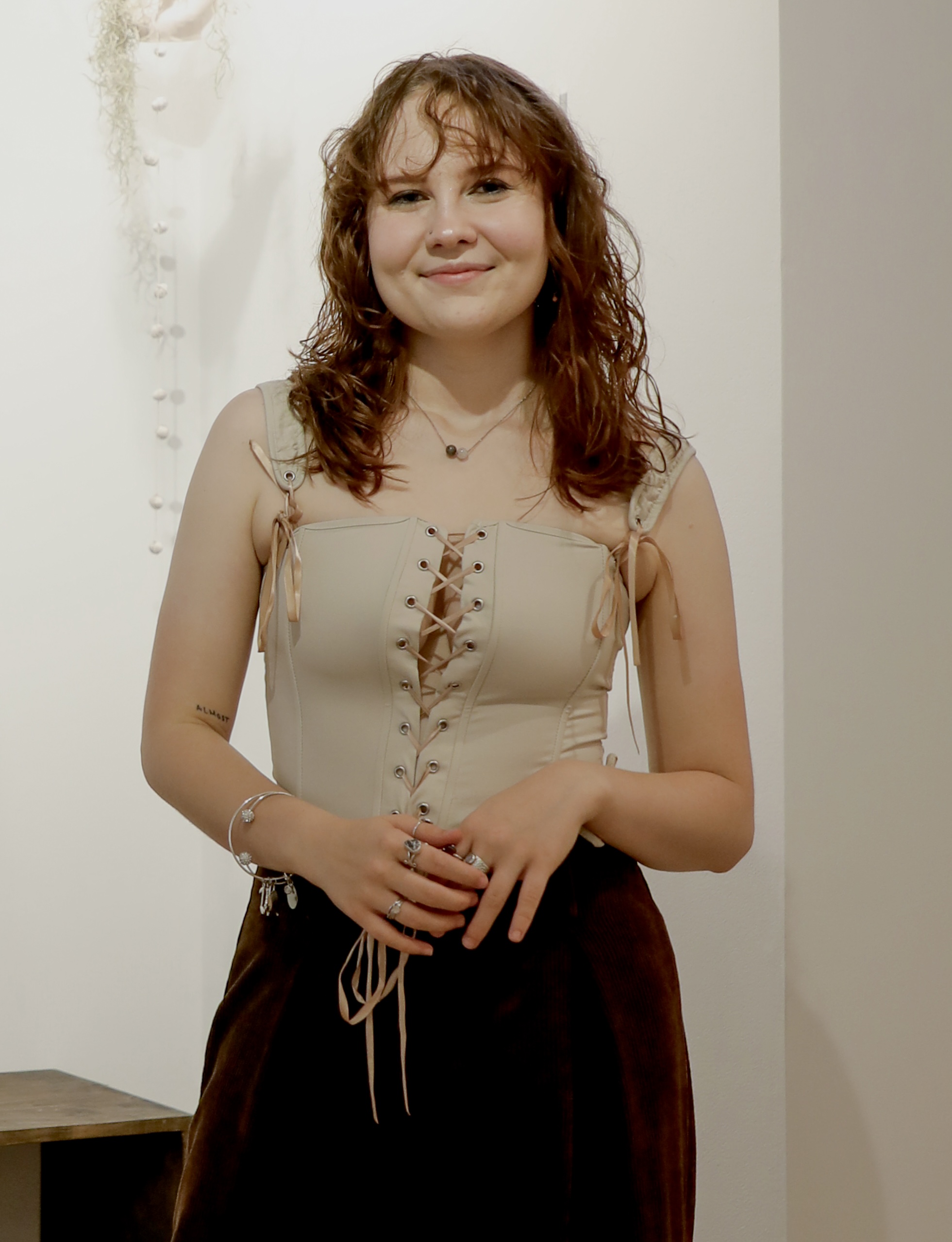 Photograph of person with long dark reddish brown hair, light beige skin, wearing a beige shirt, dark velvet skirt, and silver jewelry