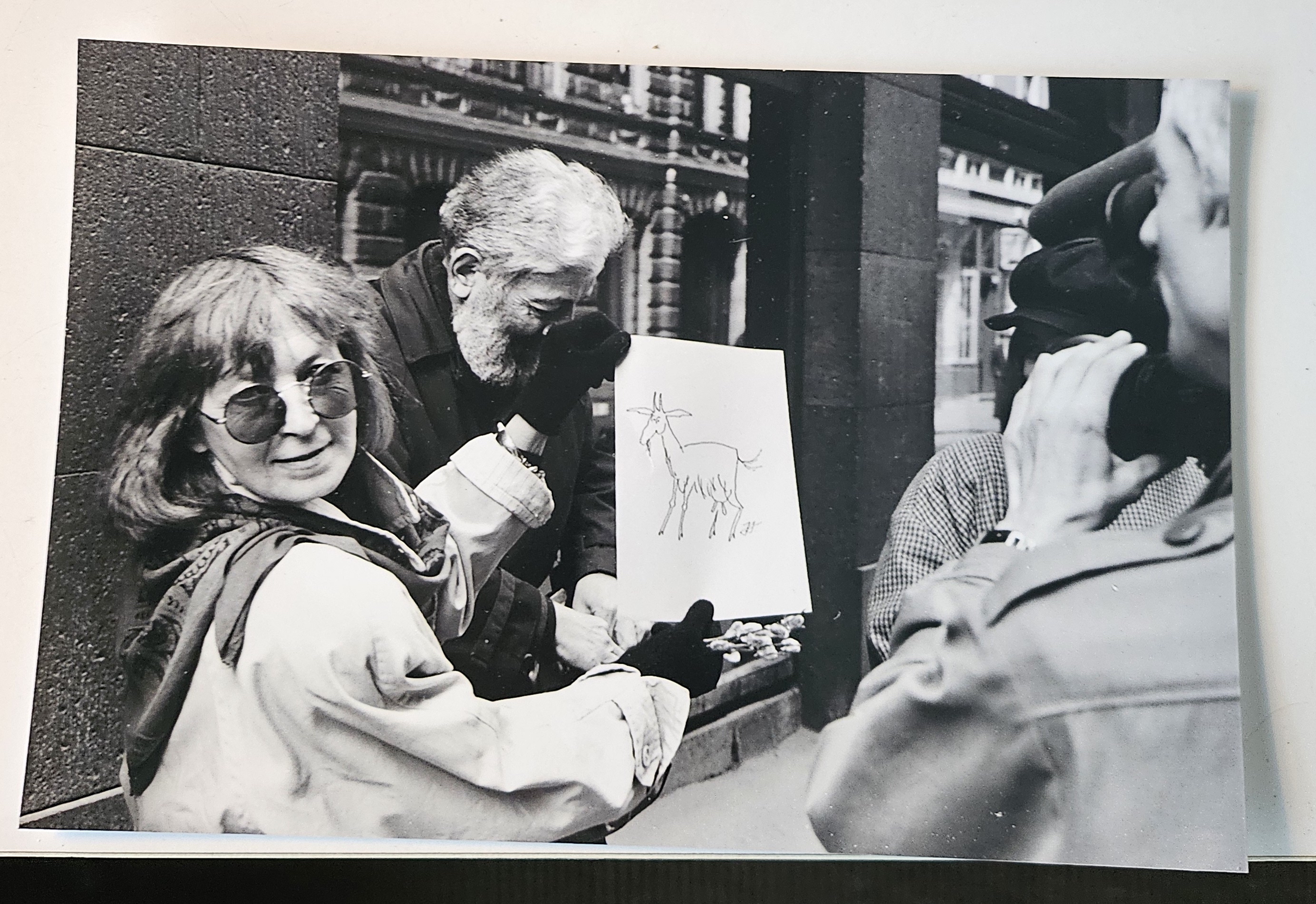 Black and white photograph of Anda holding up a drawing of a goat/Kaza.