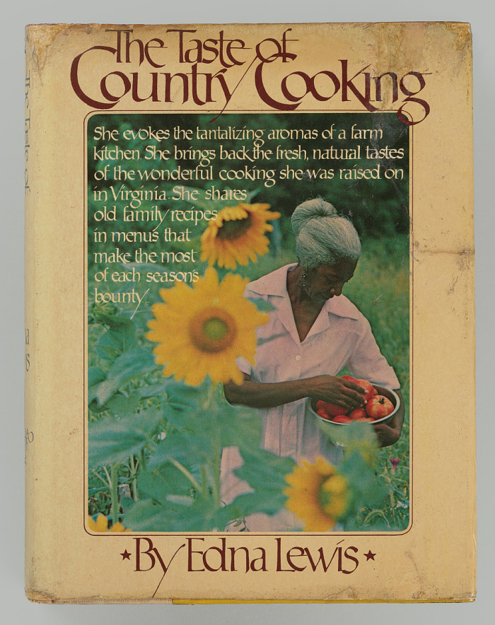 We see a a book, slightly worn around the edges. A grey-haired black woman is in focus as holds a metal bowl of bright red tomatoes. in the foreground are tall yellow sunflowers. The woman is surrounded by vegetation. This is image is surrounded by a light yellow border. Its title, in a reddish brown font, is to the top of the image, while the author is at the bottom, with two small starts on either side of her name.
