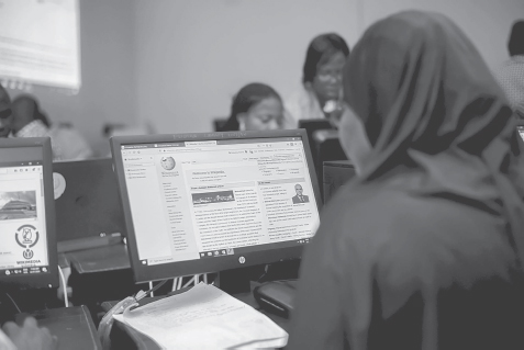 A person looking at the computer screen where it displays a Wikipedia page. In the background, there are other people looking at their desktop computers.
