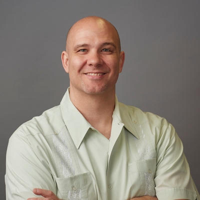 Photograph of bald person with light-colored skin, wearing a light green collared shirt with pockets
