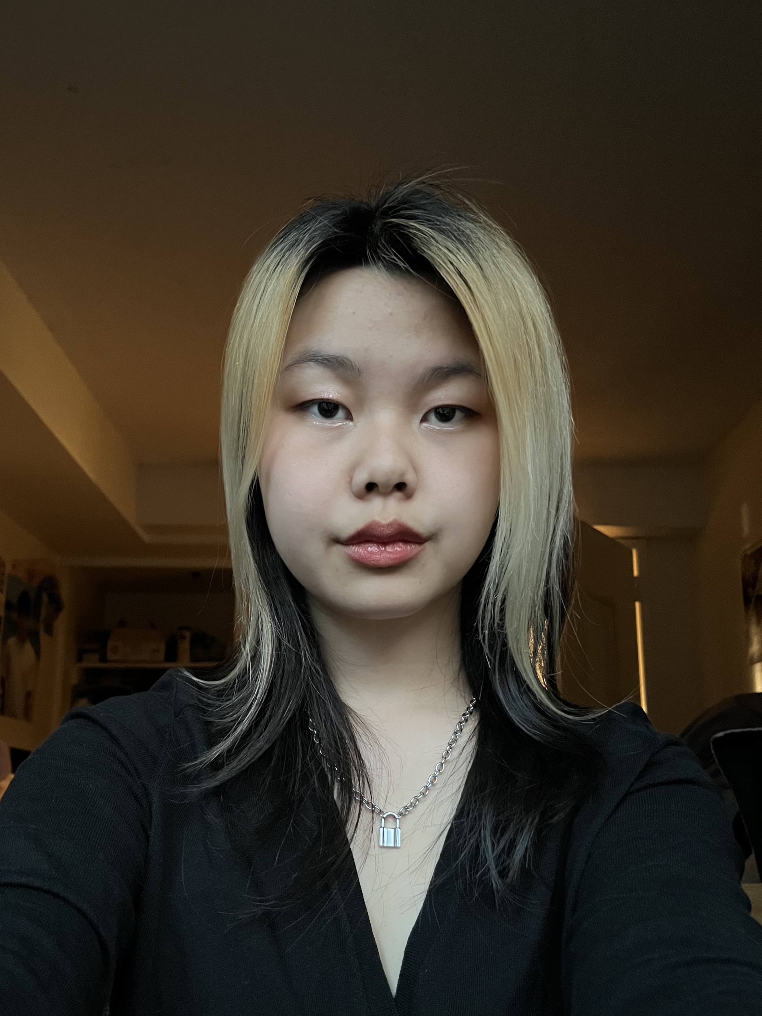 Photograph of person with long blonde and black hair, light beige skin, wearing a black shirt